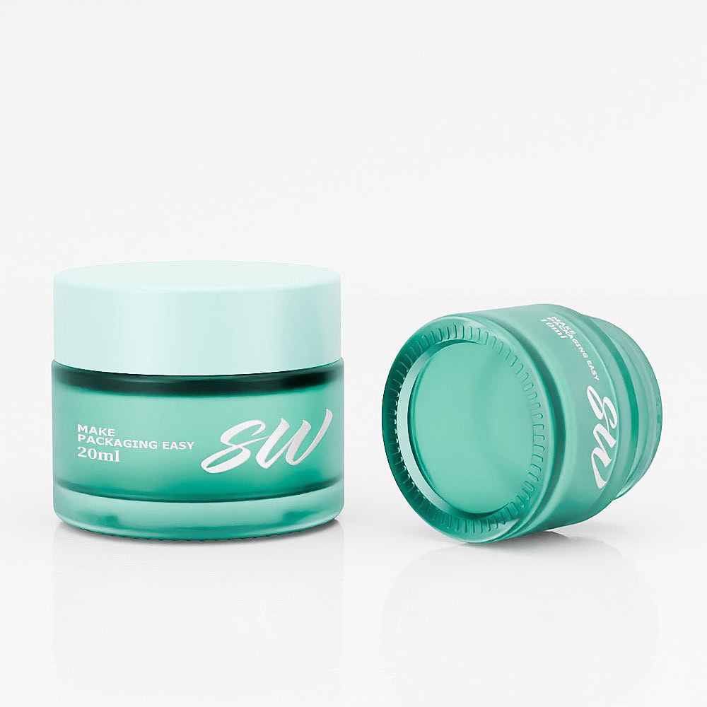 Two teal glass jars for skincare packaging, one upright and one lying down.